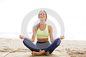 Happy young woman sitting in yoga pose at the beach