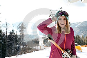 Happy young woman with ski equipment near chairlift at mountain resort, space for text