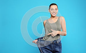 Happy young woman with slim body in oversized jeans on light blue background, space for text. Weight loss