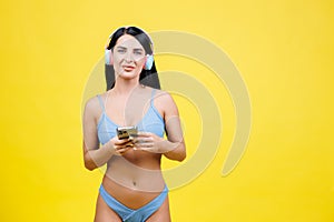Happy young woman slim body wear blue swimsuit listen music in headphones and holding mobile phone in hands isolated on yellow