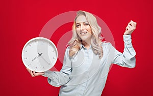 Happy young woman with smile face holding wall clock, isolated on red background. Exhilarated girl