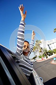 Happy young woman smiling with arms raised outside car window