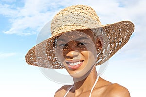 Happy young woman smiling at the beach side, wearing sun hat and bikini, portrait of African latin American woman in sunny summer