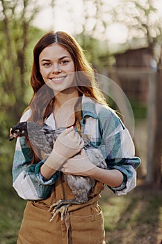 A happy young woman smiling and holding a young chicken that lays eggs for her farm