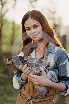 A happy young woman smiling and holding a young chicken that lays eggs for her farm