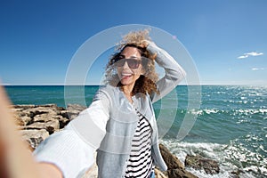 Happy young woman smiling and taking selfie by the sea
