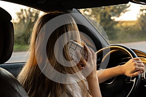 Happy young woman speaking by mobile phone while driving car. Business woman talking phone call in automobile. Unsafely