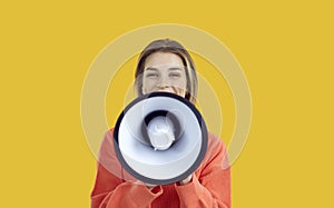 Happy young woman speaking or shouting in megaphone isolated on yellow background