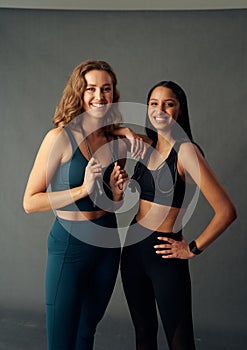 Happy young woman in sports bra holding jump rope while looking at camera with friend