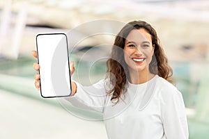 Happy Young Woman Standing In Airport And Showing Big Blank Smartphone
