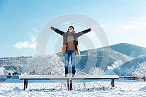 A happy young woman is standing on a bench with her arms outstretched. Winter Christmas holidays. Outdoor recreation in