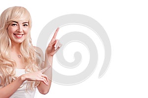 Happy young woman standing isolated over white wall background. Looking camera showing copyspace pointing. Blond young