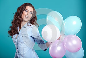 Happy young woman standing over blue wall and holding balloons.