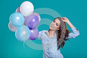 Happy young woman standing over blue wall and holding balloons.