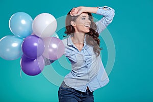 Happy young woman standing over blue wall and holding balloons.