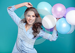 Happy young woman standing over blue wall and holding balloons.