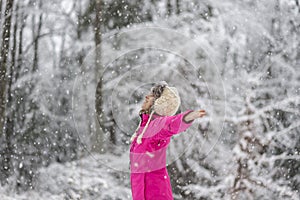 Happy young woman standing in snow blizzard with her arms spread