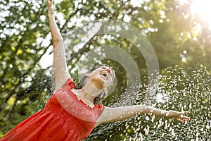 Happy young woman standing under a spray of water on a hot summ