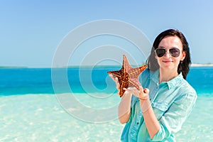 Happy young woman with starfish on white beach in in the nature reserve