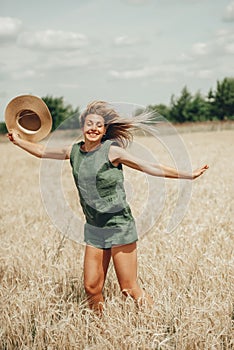 Happy young woman with straw hat in hands enjoying sun on cereal field