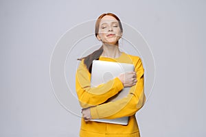 Happy young woman student holding laptop computer with closed eyes on isolated gray background.