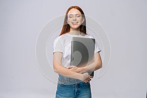 Happy young woman student holding laptop computer with closed eyes on isolated gray background.
