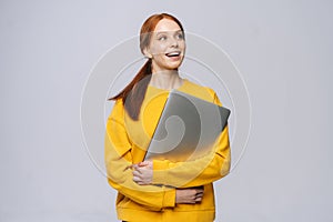 Happy young woman student holding laptop computer and looking away on isolated gray background.