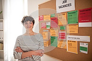 Happy young woman student standing in front of employment noticeboard.