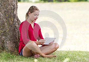 Happy young woman studying on wireless tablet sitting on grass