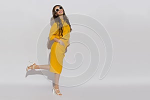 Happy young woman in sunglasses, linen shirt, shorts and high heels poses on a one leg