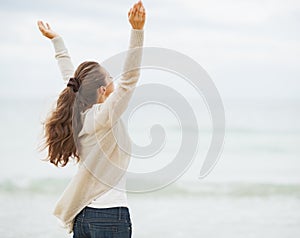 Happy young woman in sweater rejoicing on beach . rear view