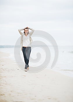 Happy young woman in sweater walking on lonely beach