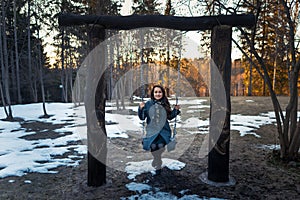 Happy young woman swinging on a swing have fun and smiling in the park in sunny winter day. One Person.