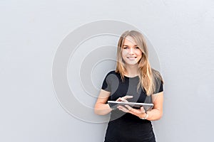 Happy young woman on the tablet by the wall