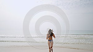 Happy young woman taking dress off and running into sea. Slim smiling brunette runs, turns in sea water waves. Fitted