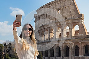 Happy young woman taking a selfie in front of the colosseum while in Rome, Italy