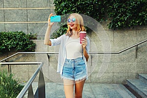 Happy young woman taking selfie picture by smartphone with coffee cup