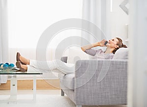 Happy young woman talking cell phone while sitting on sofa
