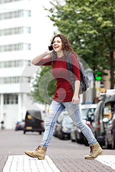 Happy young woman talking on mobile phone and crossing a road