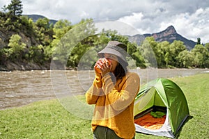 Happy young woman in the tent drinking warm tea or coffee camping in the mountains, adventure lifestyle