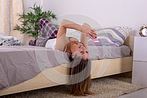 Happy young woman texting with her phone upside down in bed