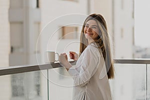 Happy young woman thinking and looking away with cup of tea or coffee with blurred city background.