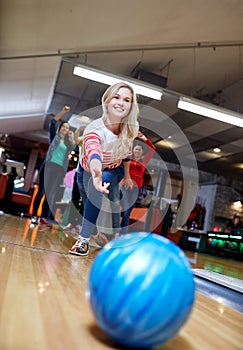 Happy young woman throwing ball in bowling club