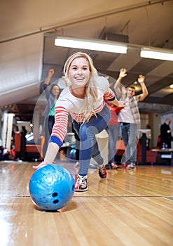 Happy young woman throwing ball in bowling club