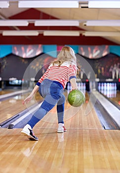 Happy young woman throwing ball in bowling club