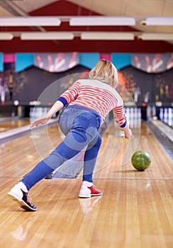 Happy young woman throwing ball in bowling club