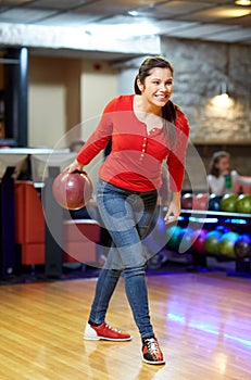 Happy young woman throwing ball in bowling club