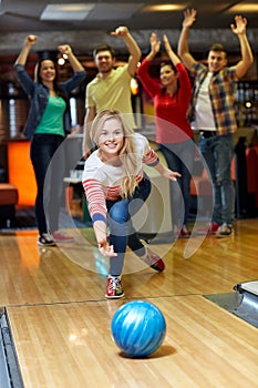 Happy young woman throwing ball in bowling club