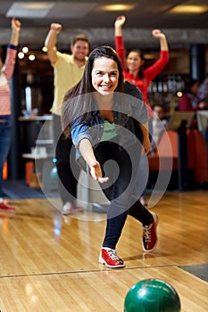 Happy young woman throwing ball in bowling club