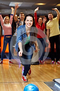 Happy young woman throwing ball in bowling club